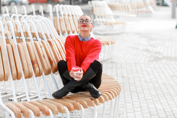 戴着眼镜，穿着红色毛衣，涂着红色口红的漂亮女人拿着一杯咖啡走在街上图片下载