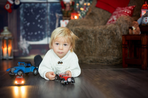 可爱的蹒跚学步的小男孩，坐在许多汽车玩具的地上，玩着图片下载