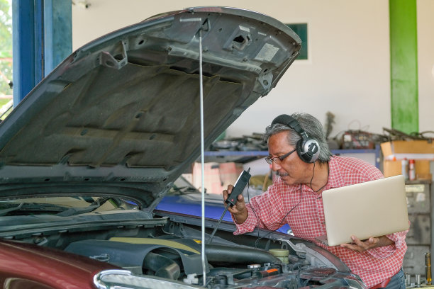 亚洲汽车技师与红衬衫使用电子工具和笔记本电脑检查汽车发动机的部分在车库引擎盖附近图片下载
