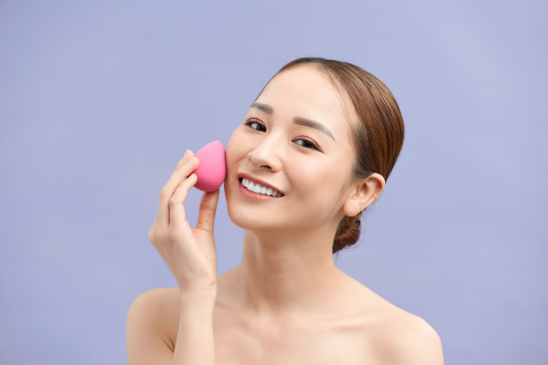 美丽的年轻女子使用美容海绵化妆。图片下载