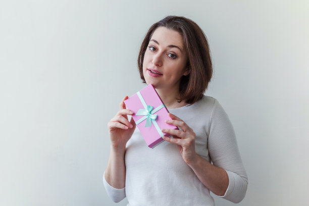 年轻的积极妇女拿着小粉红色礼盒孤立在白色背景。为假期做准备。女孩看起来又高兴又兴奋图片下载