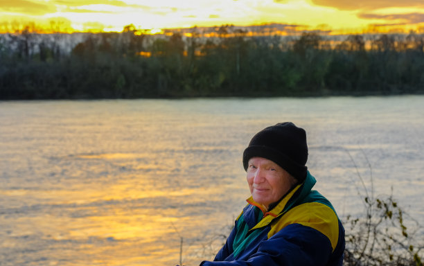 在秋天日落时，一位老人坐在河边图片下载