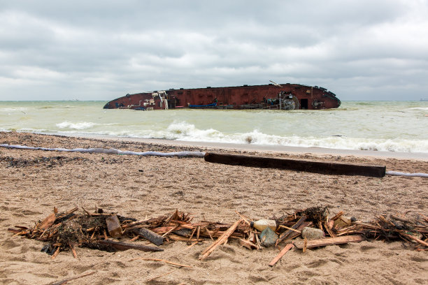 一艘油轮在沙滩上失事的后果是一个保护屏障和垃圾的残余物破碎了木板。图片下载
