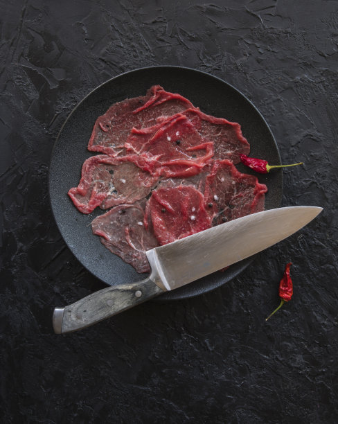 大理石般花纹的牛肉薄片配以柠檬、橄榄油和帕玛森奶酪，背景是黑色的石板。顶视图，带有复制空间图片下载