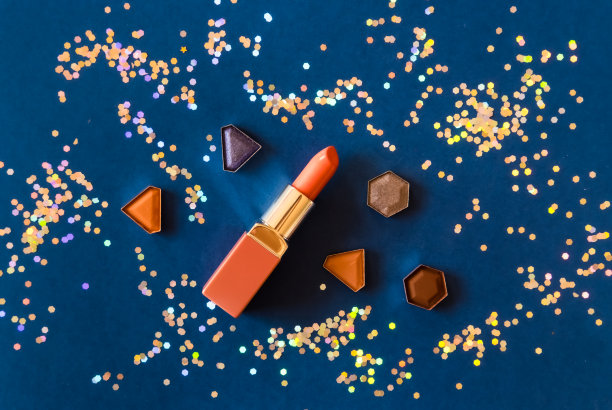 珊瑚色口红，眼影和金色闪粉在深蓝色的背景。化妆品的概念。图片下载