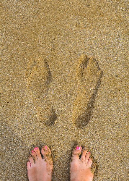 光着脚的女人的脚上有一个红色的足疗旁边自己的脚印在潮湿的黄色的沙子图片下载