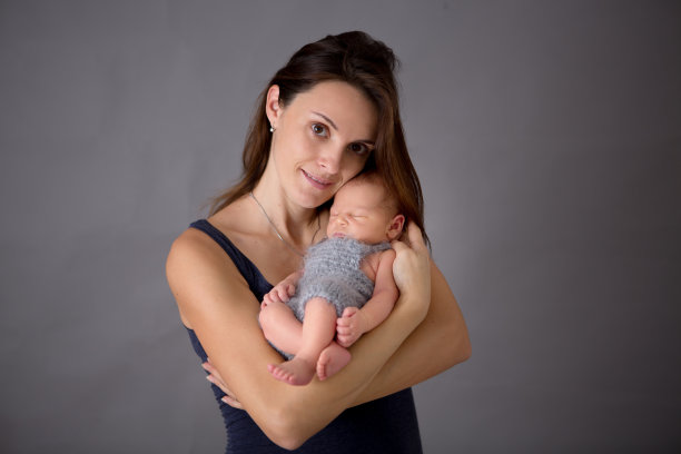 母亲在灰色的背景下亲吻和拥抱新生的儿子，温柔，关心，爱图片下载