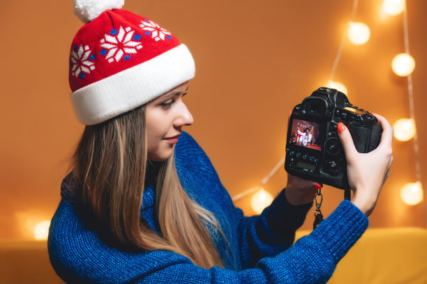 美丽的女人戴着圣诞帽和专业数码相机在咖啡馆图片下载