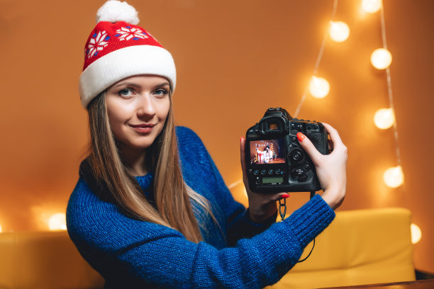 美丽的女人戴着圣诞帽和专业数码相机在咖啡馆图片下载