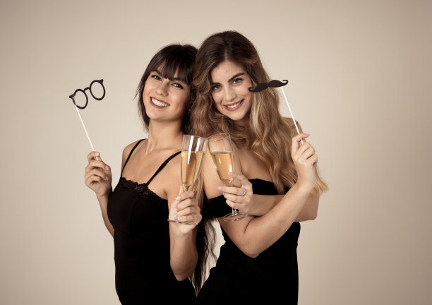 两个美丽的女朋友开心地庆祝圣诞节或新年前夜举杯祝酒。女性们穿着时尚性感的派对礼服，喝着香槟。人们的友谊和庆祝。图片下载