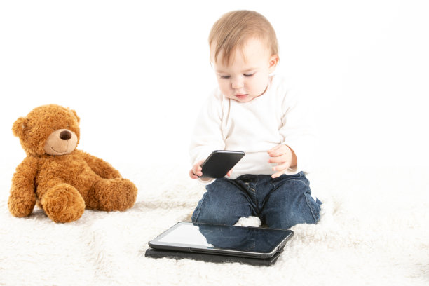 宝宝在玩平板电脑和手机，背景是一只泰迪熊图片下载