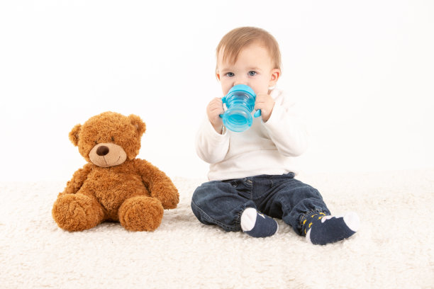 手里拿着水壶的婴儿，身边放着一只泰迪熊。图片下载