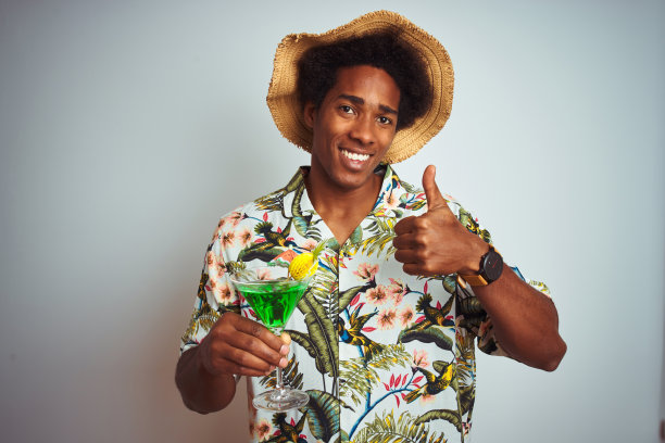 非洲裔男子在假日戴着夏天的帽子喝鸡尾酒在孤立的白色背景下开心地笑着做ok手势，用手指竖起大拇指，优秀的手势图片下载