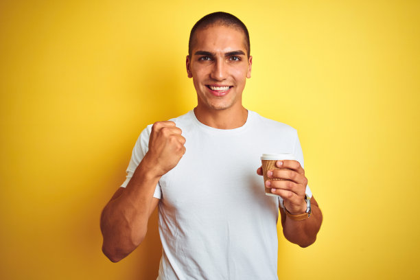 年轻英俊的男子喝着带走的一杯咖啡越过黄色孤立的背景尖叫自豪，庆祝胜利和成功非常兴奋，欢呼的情绪图片下载