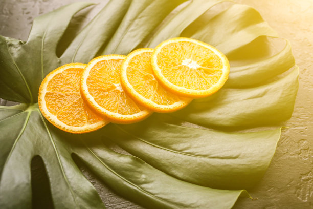 绿色热带叶子上的橙子。怪物室内植物在黑色的背景。生态友好的照片。图片下载