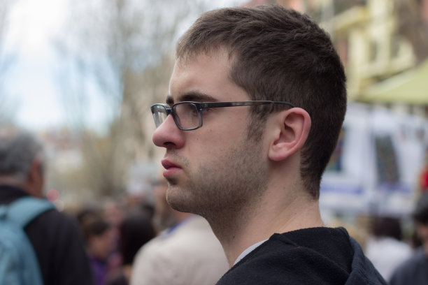 一名年轻的白人男子，一头卷发，戴着眼镜，站在城市的街道上。图片下载