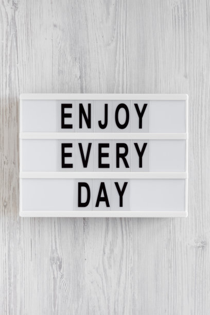 “享受每一天”的字样写在灯箱上，白色木质背景，俯视图。头顶上，从上面看，是平躺着的。图片下载