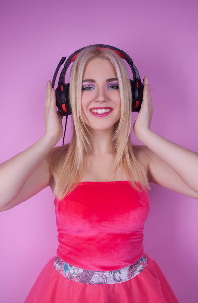 一个美丽快乐的金发女孩的近距离肖像听音乐耳机和他们与她的手图片下载