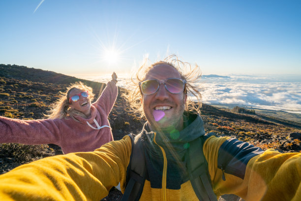 快乐的年轻夫妇在夏威夷火山上云端之上自拍，欣赏日落美景图片下载