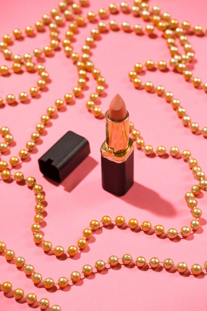 裸色唇膏以粉色背景装饰金色节日珠子。图片下载