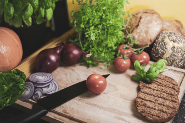 一个素食汉堡的配料放在一块木板上，配上西红柿和一把刀图片下载