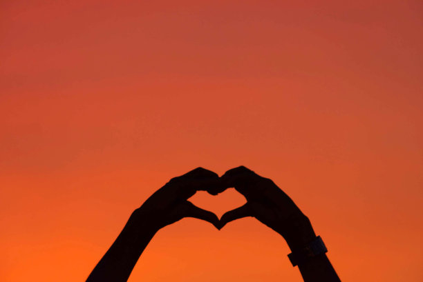 一颗心形手的黑色剪影背景天空中夕阳的橙色光芒。图片下载