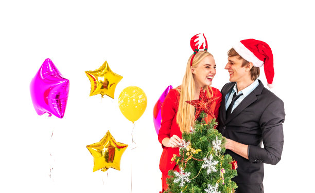 在庆祝新年的晚会上，一对年轻幸福的夫妇喜欢与彩色气球和圣诞树摆pose图片下载
