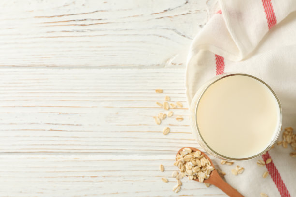 一杯燕麦牛奶，一勺燕麦籽和餐巾纸放在白色木质背景上，俯视图。空间的文本图片下载