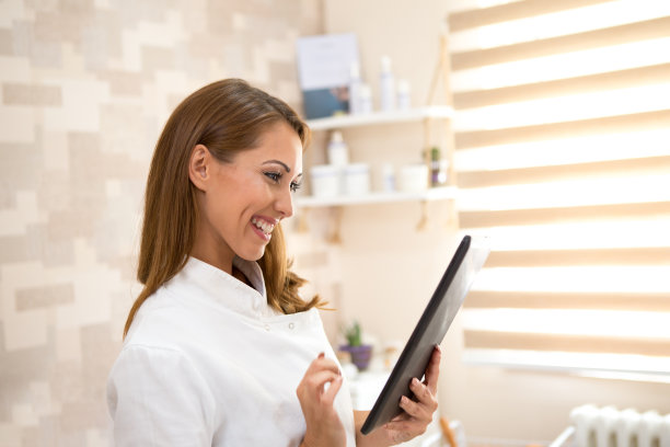 一位年轻漂亮的黑发护士很高兴地用手中的平板电脑检查病人的健康状况。图片下载