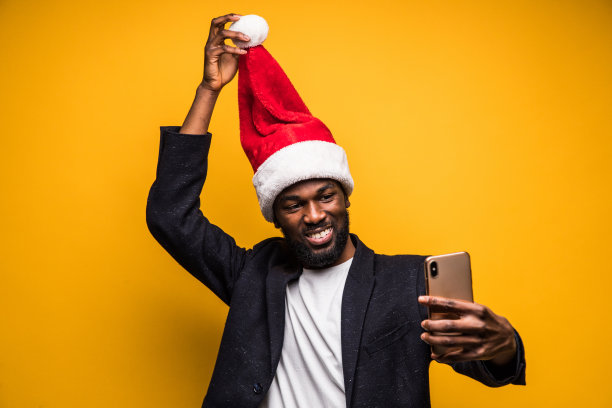 年轻英俊的非洲男子在圣诞老人帽自拍手机孤立在黄色背景图片下载