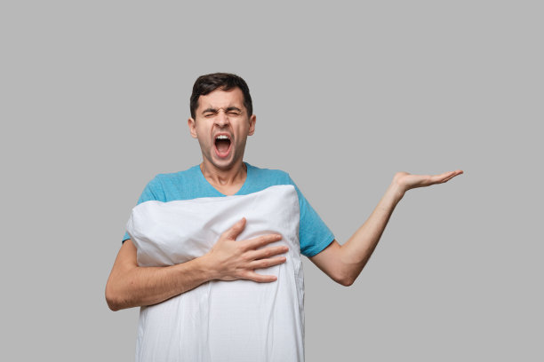 一个穿着蓝色t恤的疲惫的黑发男人躺在一个白色的枕头上，灰色的背景孤立无援图片下载