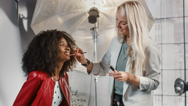 后台的照片拍摄:化妆师应用化妆在美丽的黑色模特。时尚杂志摄影工作室图片下载