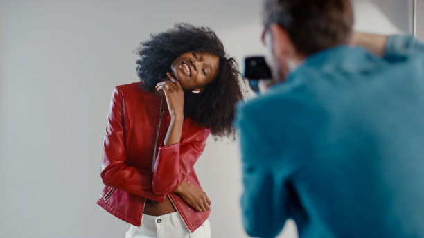 幕后照片拍摄:美丽的黑色模特为摄影师摆姿势，他用专业相机拍照。时尚时尚杂志照片拍摄与专业设备在一个工作室图片下载