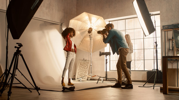 美丽的黑色模特为摄影师摆姿势，他用专业相机拍照。她玩面部表情。时尚时尚杂志照片拍摄在一个工作室。黄金小时拍摄图片下载