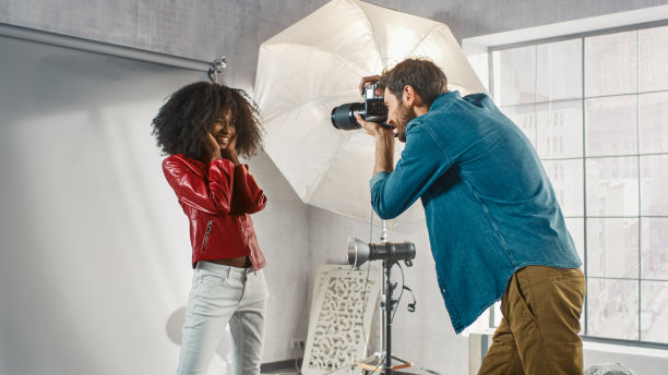 幕后照片拍摄:美丽的黑色模特为摄影师摆姿势，他用专业相机拍照。时尚时尚杂志照片拍摄与专业设备在一个工作室图片下载