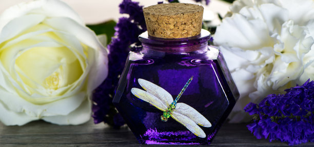 紫色玻璃瓶与古董软木盖和蜻蜓图片上的木板。有白色和紫色花朵的玻璃容器图片下载