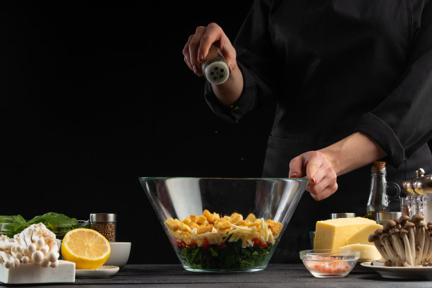 厨师在沙拉中撒上意大利调味料。静止，沙拉，有机食材和产品。素食和美味的食物。黑色背景上的食物广告照片，有设计空间图片下载