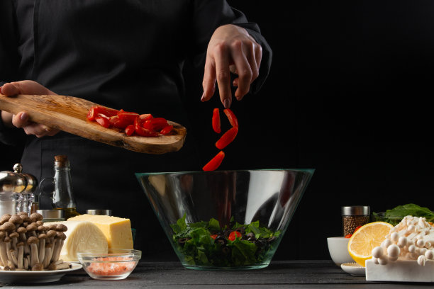 厨师把圣女果和沙拉一起倒进碗里。沙拉、有机食材及产品。素食和美味的食物。食品广告照片，以黑色为背景图片下载