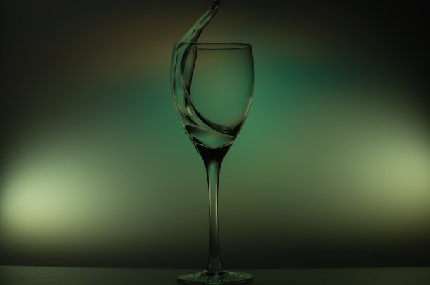 水倒进玻璃杯里。水溅在玻璃上发光的背景。透明液体溅在酒杯中图片下载