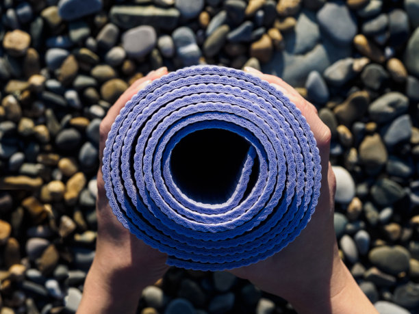 女人手中的瑜伽垫卷起来。海滩上的石头图片下载