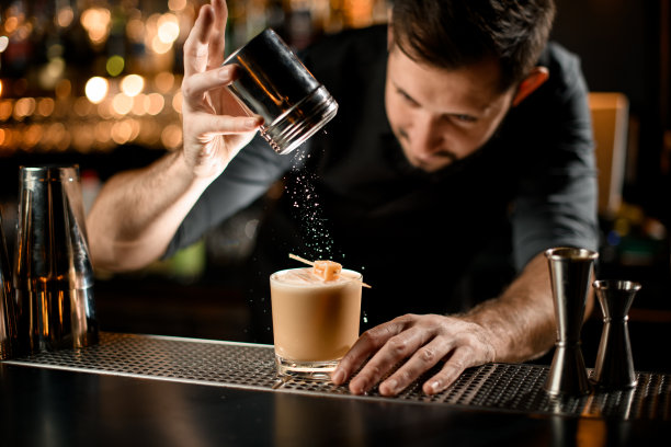 酒保在酒精鸡尾酒中洒上酸味混合物和糖果图片下载