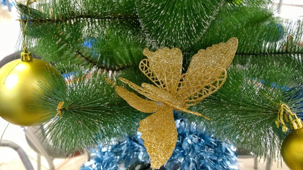 新年背景快乐。圣诞树装饰品:闪亮的金色蝴蝶和闪闪发光的球。传统的圣诞装饰和人造冷杉树。假期的心情。设计室内，想法和灵感。图片下载
