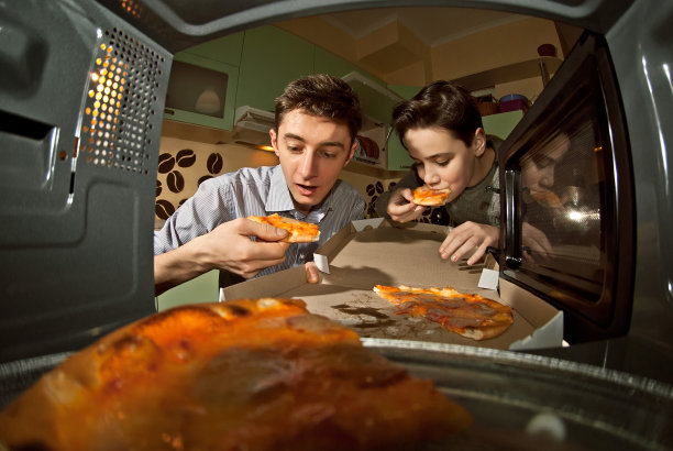 他们从微波炉里拿披萨。在家庭厨房加热食物。快餐。微波中视图。在家做饭。披萨和汉堡从烤箱中取出。男人吃比萨饼。图片下载