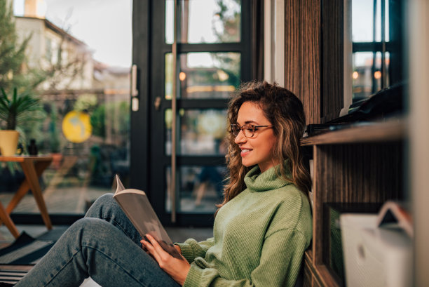 一个年轻女人在家里放松，阅读的侧面肖像。图片下载
