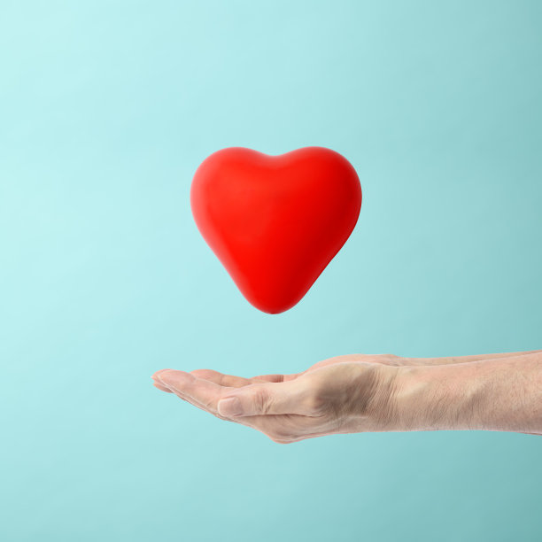 在淡蓝色的背景下，一只手漂浮着一个红色的心形图片下载