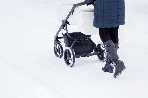 年轻的母亲推着婴儿车在雪道上。在暴风雪过后的冬日里，一个女人走在白色的雪地里。背面视图。特写镜头。图片下载