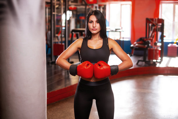 在体育馆里，年轻的女拳击手站在拳击袋附近图片下载