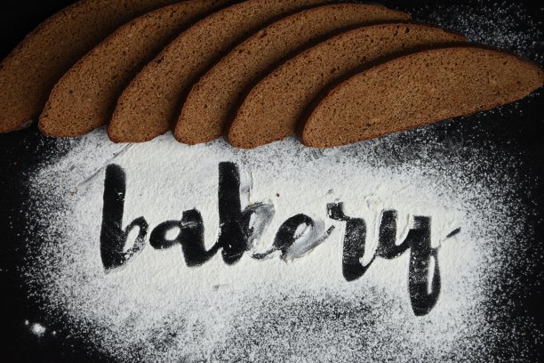 题字面包房在白面粉上撒黑麦切片面包在深色的背景上，用面粉手记上面包房的字样图片下载