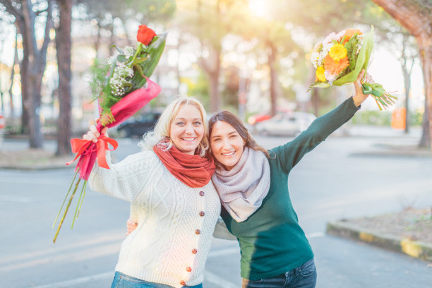两个快乐的女人手里拿着鲜花，微笑着看着镜头——母亲和女儿在一起玩——春天和妇女节庆祝概念图片下载
