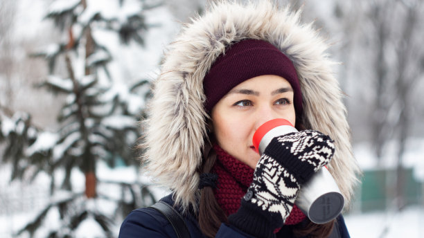 美丽的年轻女孩喜欢在冬天的公园里散步时用保温瓶喝咖啡。图片下载